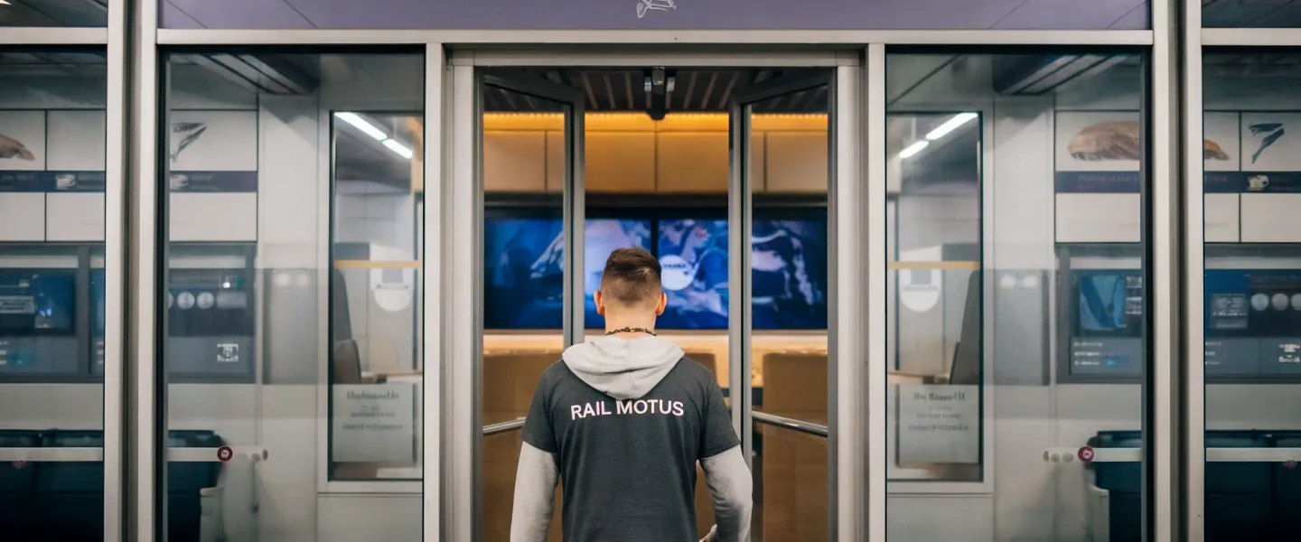 Man in Rail Motus shirt entering First Class Lounge at European train station, showcasing Interrail Pass perks