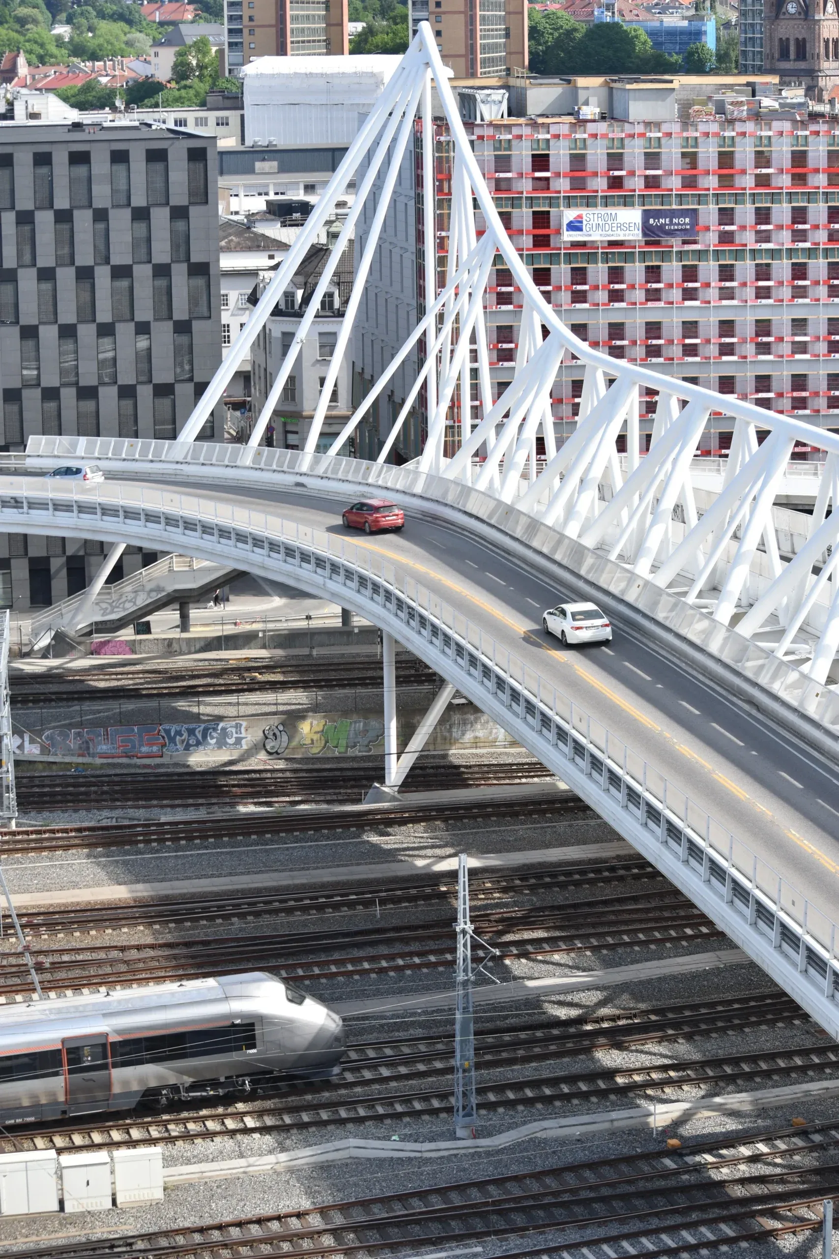 A modern bridge crossing over railway tracks at Oslo Central Station, with urban buildings in the background.
