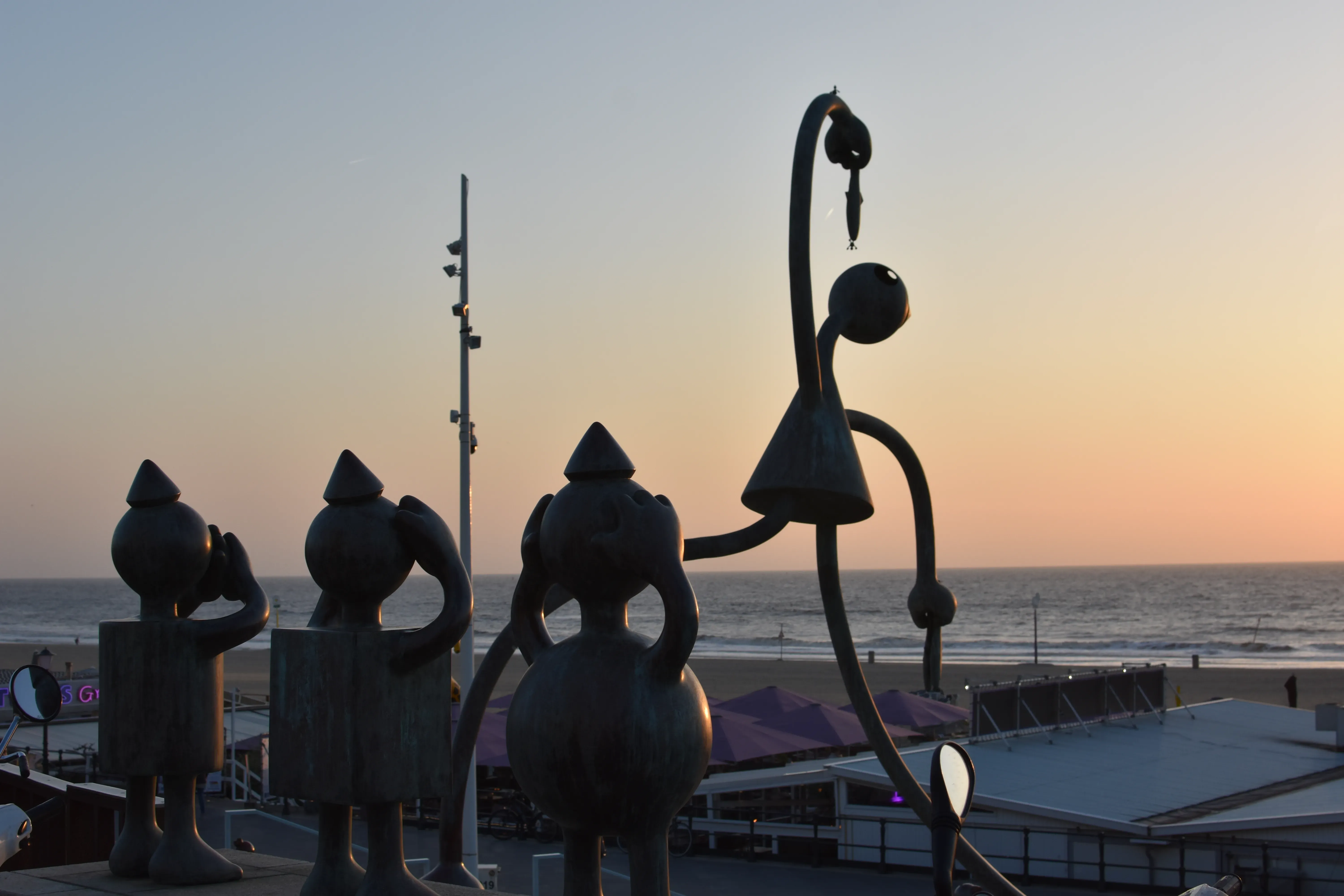 Abstract sculptures at The Hague beach, silhouetted against a vibrant sunset.