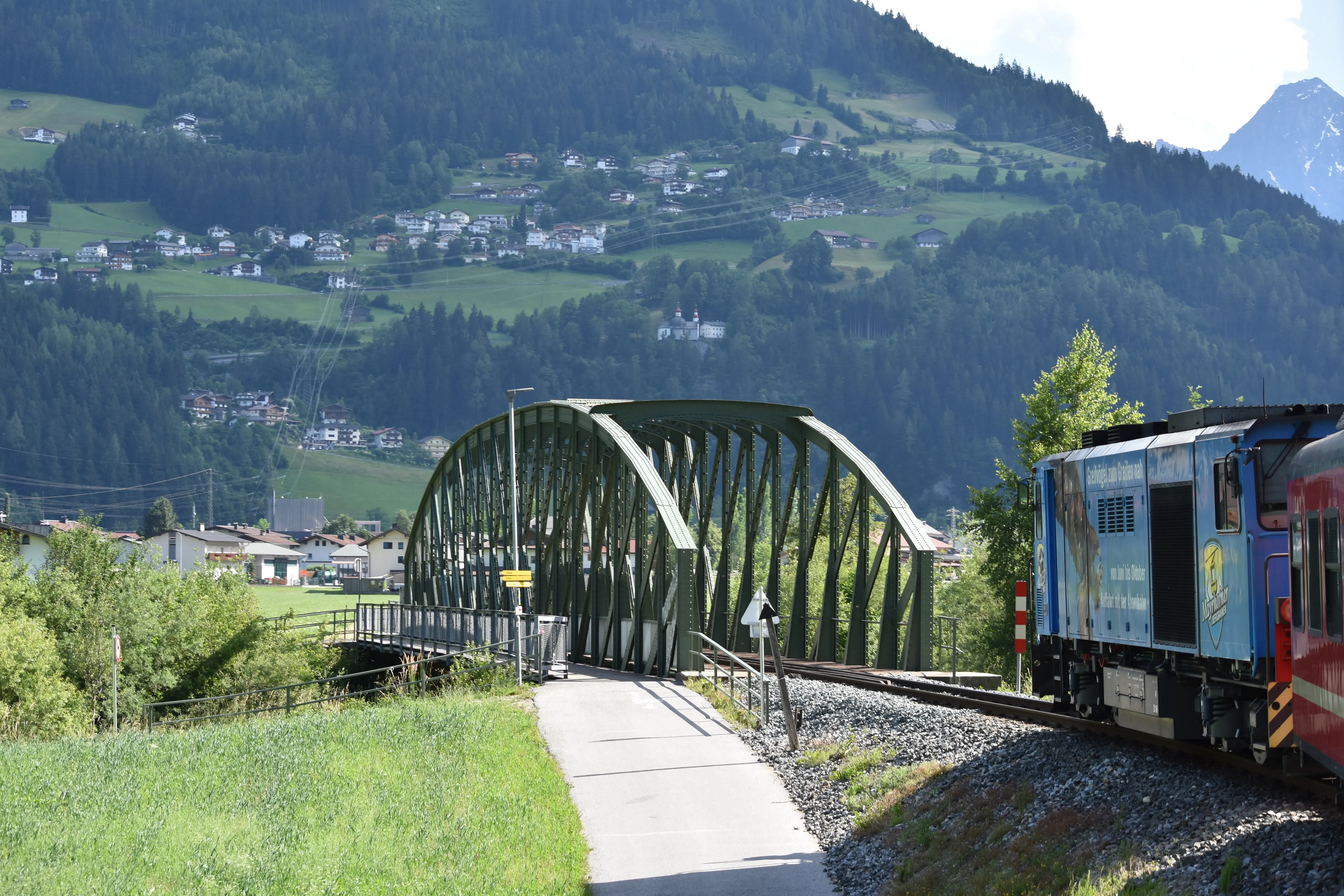 Zillertalbahn train traveling through the Austrian Alps, with a scenic bridge and mountains in the background.